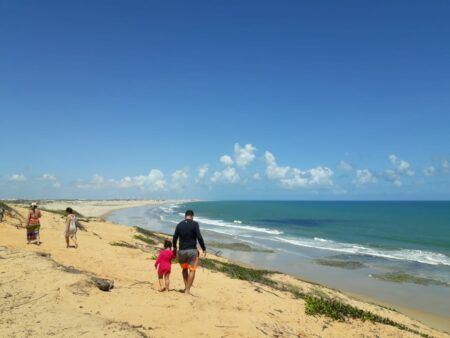 Família caminhando e vista panorâmica da praia de Lagoinha no fundo