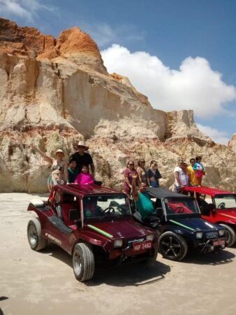 Grupo de pessoas em três buggys na praia com falésias atrás