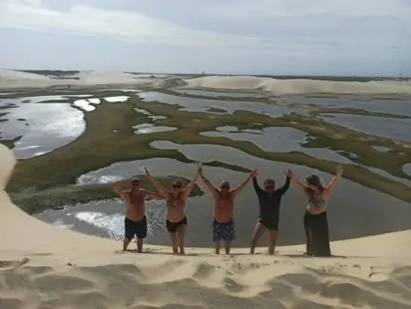 Pessoas tirando foto em uma duna com as mãos pra cima