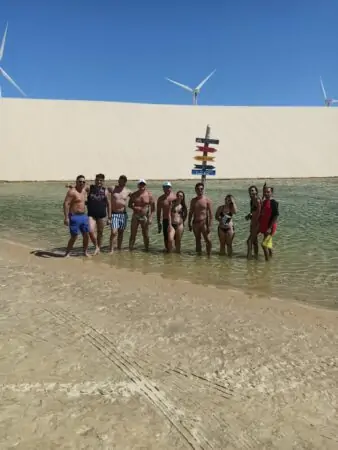 Pessoas num lago entre as dunas com geradores eólicos ao fundo