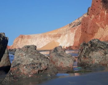 Grandes pedras na beira do mar com falésias ao fundo