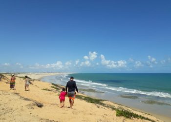 Família caminhando e vista panorâmica da praia de Lagoinha no fundo