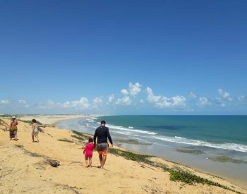 Família caminhando e vista panorâmica da praia de Lagoinha no fundo