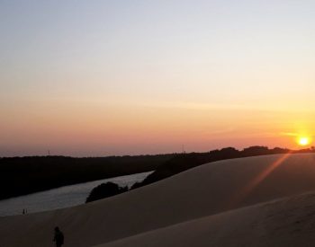 Uma pessoa na duna com um rio de fundo e por do sol