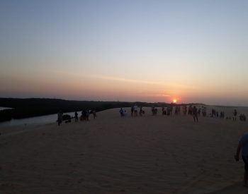 Pessoas vendo o pôr do sol numa duna