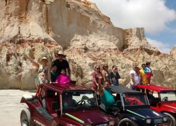Grupo de pessoas em três buggys na praia com falésias atrás