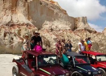 Grupo de pessoas em três buggys na praia com falésias atrás