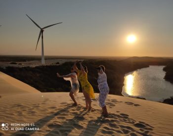Três mulheres tirando foto na duna com pôr sol de fundo
